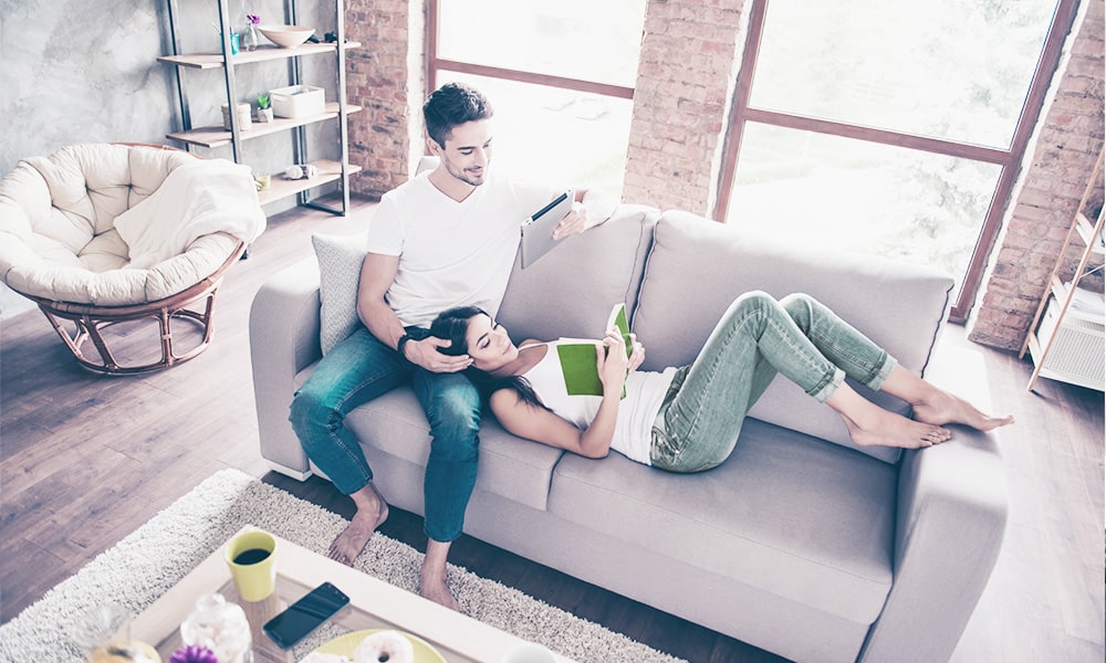 Couple lays on couch while on iPad and reading
