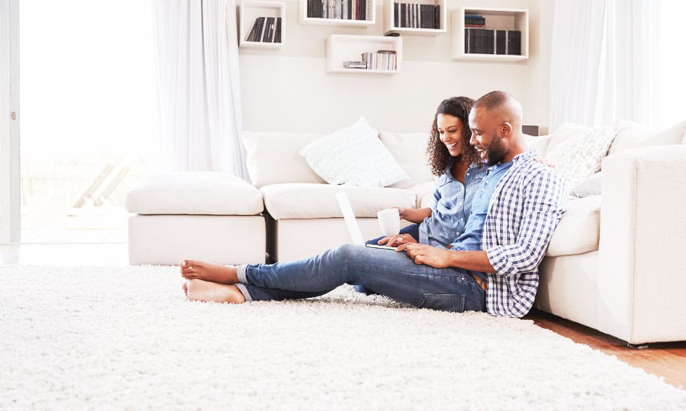 Middle aged couple laying against couch while on computer and holding mug